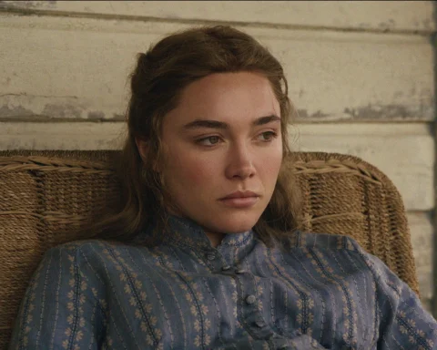 "A young woman in a blue patterned dress sits pensively in a wicker chair against a worn wooden wall, appearing thoughtful and somber in a rustic, vintage setting."